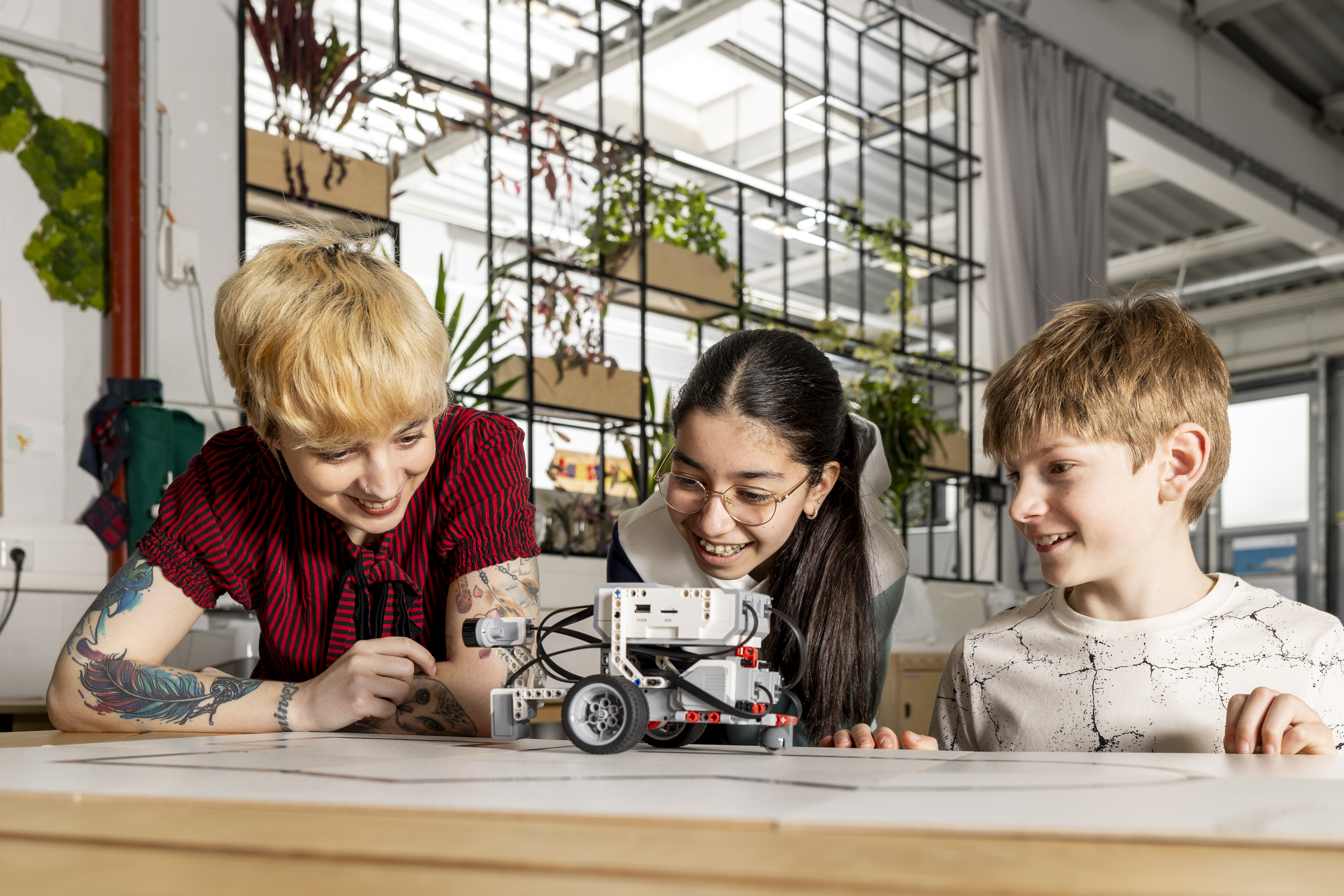 Drei Personen beobachten gespannt einen fahrenden Roboter