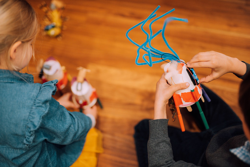 Ein Plastikbecher, der mit Stohhälmen beklebt wurde und an dem eine Batterie zu sehen ist wird festgehalten